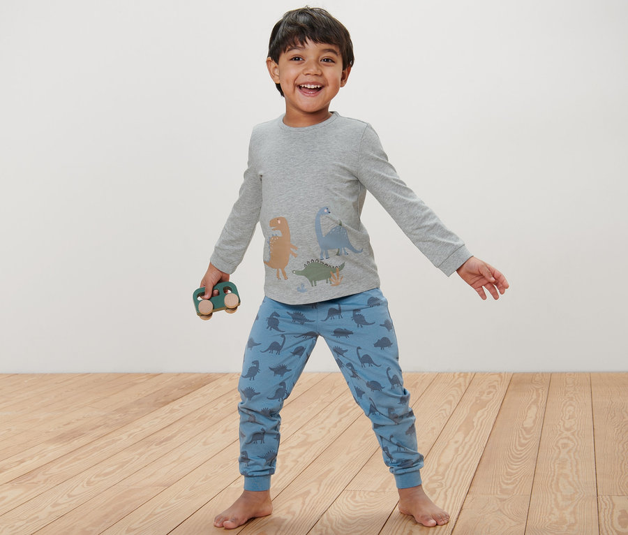Junge trägt blauen Kinder-Pyjama mit Dinosauriern und hält ein Holzauto.