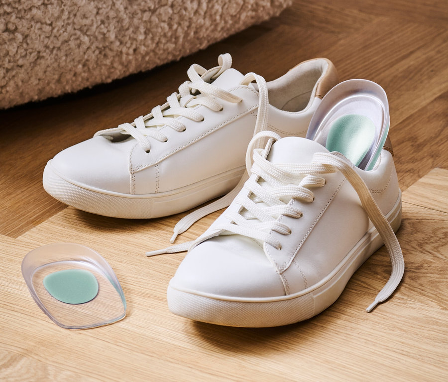 Zwei weiße Turnschuhe und ein Paar Fersenkeile auf einem Holzboden.