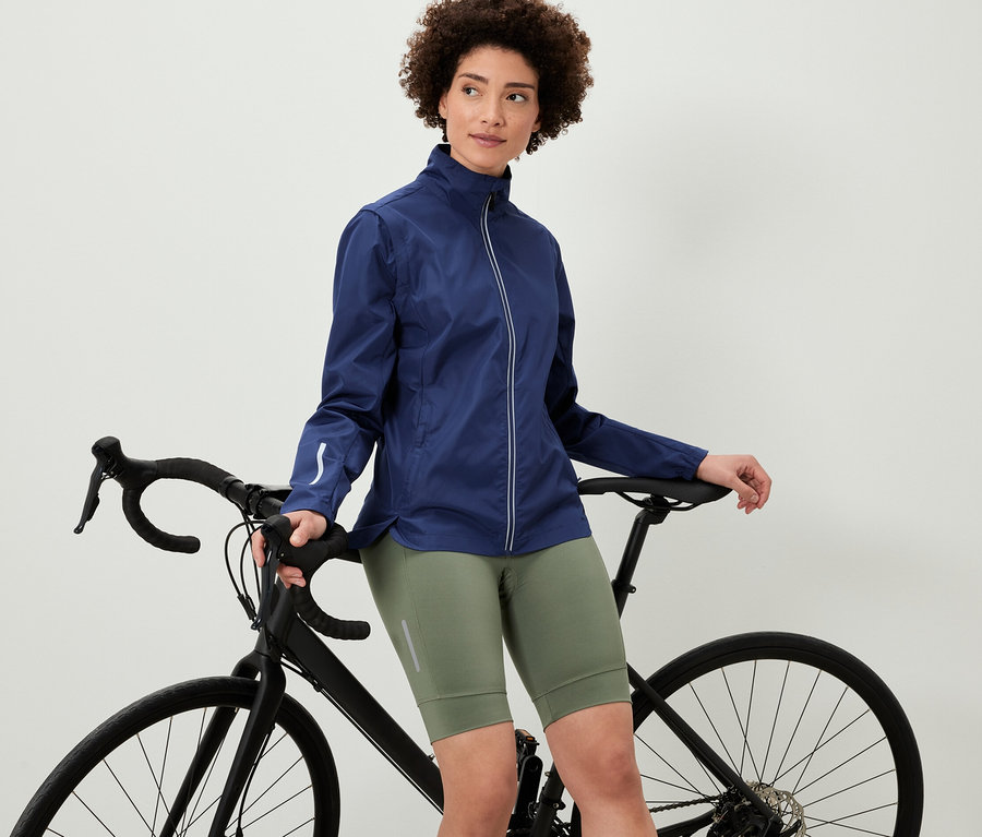 Frau, die sich an ein Fahrrad lehnt, trägt eine 2-in-1-Fahrradjacke.