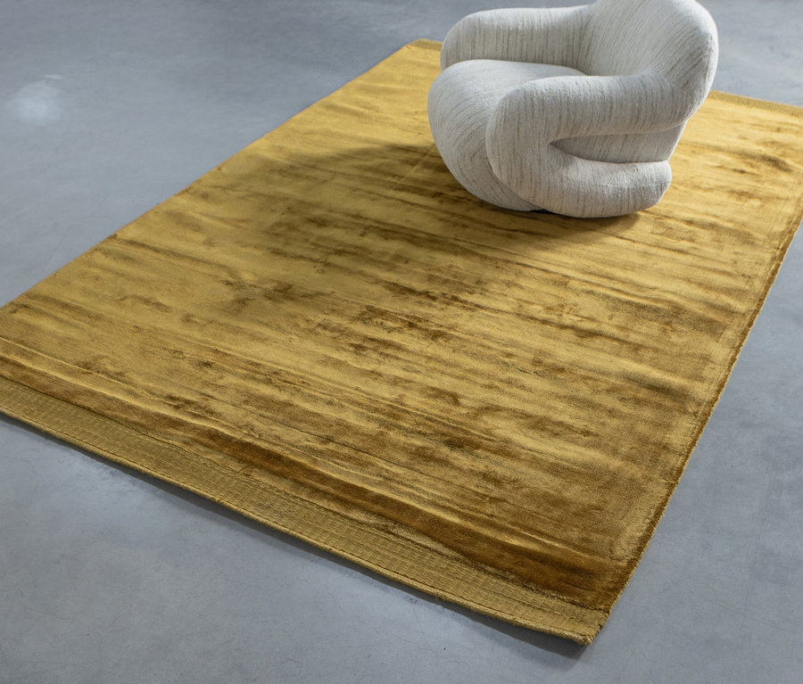 Ein beiger Sessel steht auf dem honiggelben Teppich »Tammo« von Woood.