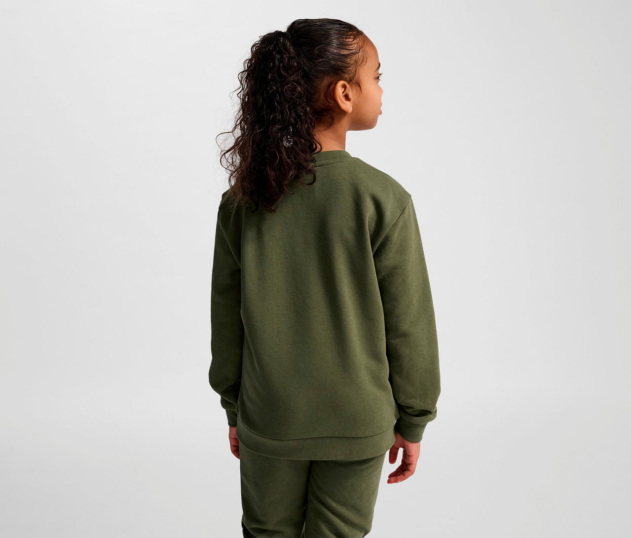 Mädchen steht mit dem Rücken zur Kamera und trägt ein grünes HUMMEL HMLJR Base-Sweatshirt.