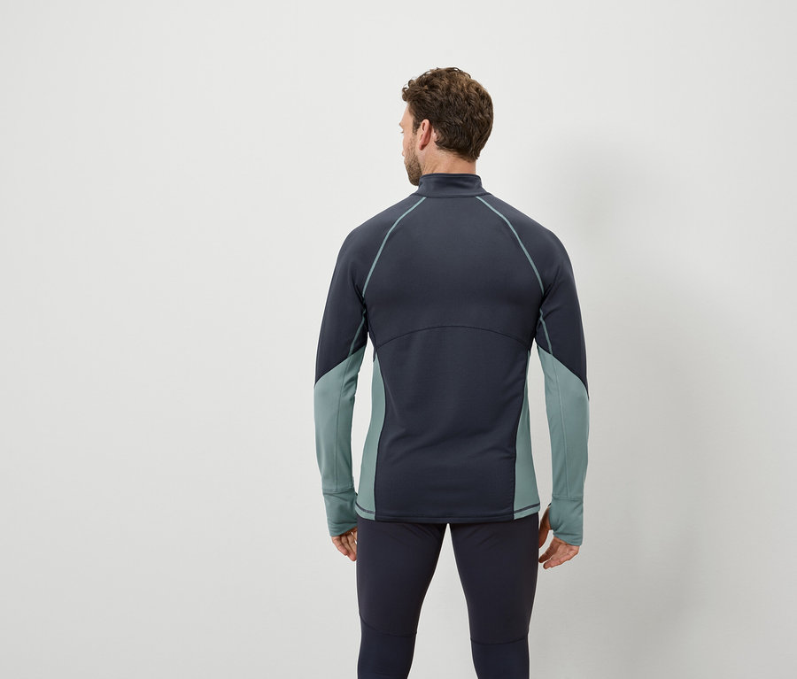 Mann von hinten trägt ein dunkelblaues Langarmshirt mit blaugrünen Einsätzen und dunkelblaue Leggings.