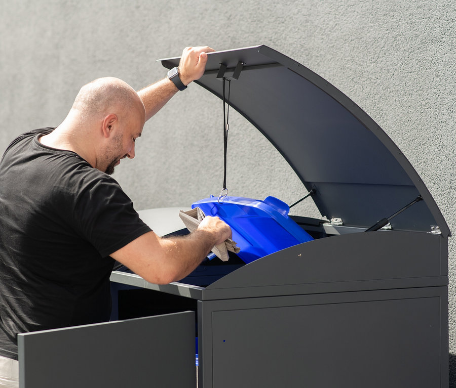 Mann stellt blaue Mülltonne in 3er Mülltonnenbox.