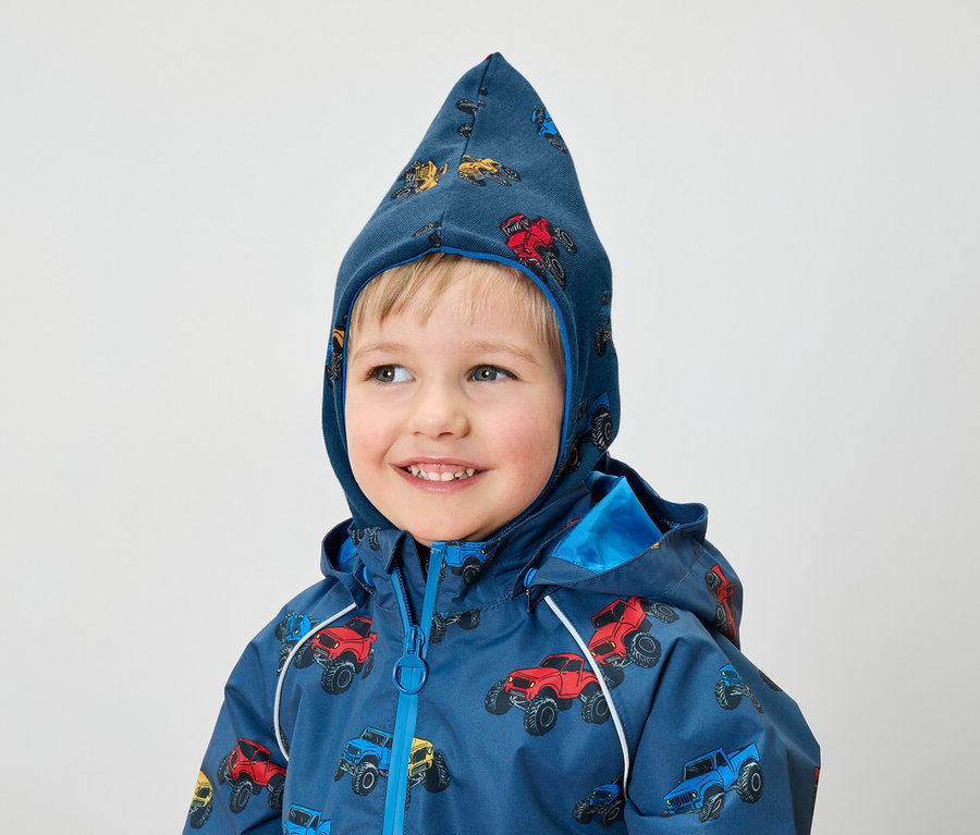 Ein lächelnder Junge trägt eine blaue Jacke und eine Kapuze mit Monster-Truck-Aufdruck.