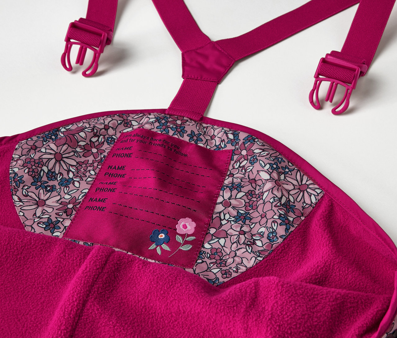Detail einer Kinder-Thermo-Regenhose, geblümt, einschließlich Details wie Hosenträger und Namensschild.