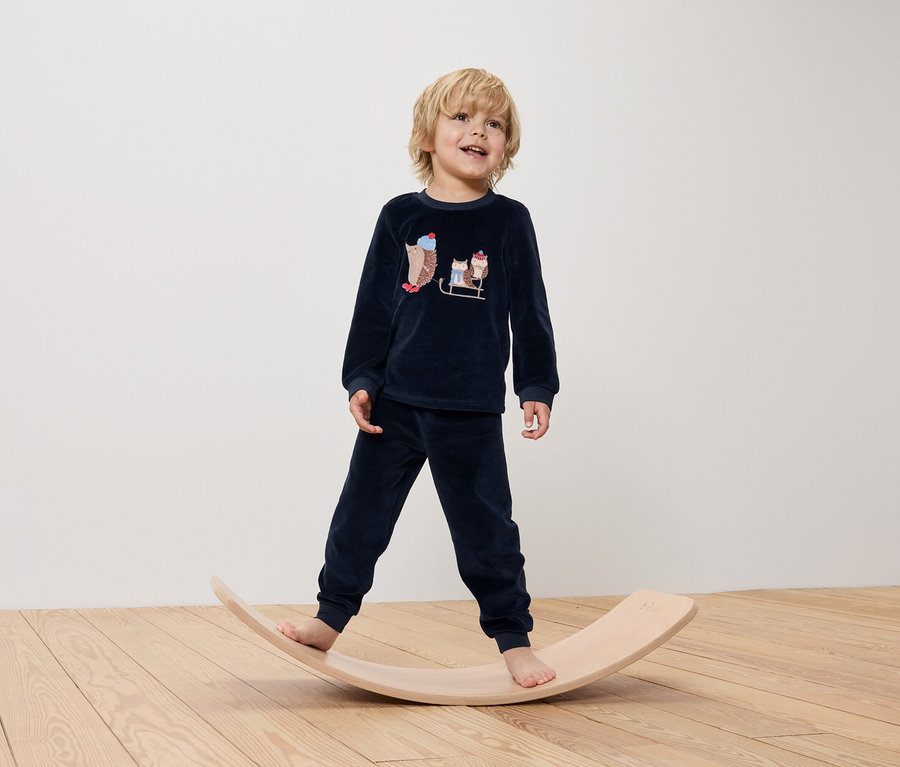 Junge im blauen Pyjama mit Igeln steht auf einem hölzernen Balancebrett.