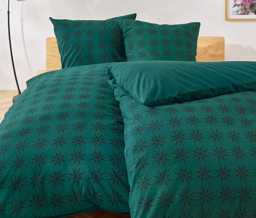 Grüne Bettwäsche mit dunklem Blumenmuster auf einem Bett.