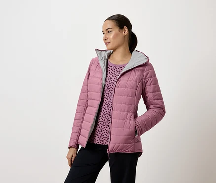 Frau trägt eine rosa Steppjacke mit Kapuze und marineblaue Hosen, sie schaut nach links.