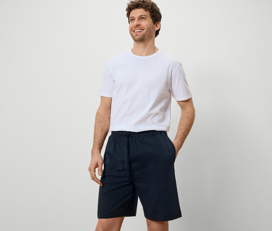 Mann mit weißem T-Shirt und marineblauen 2 Pyjamashorts vor einem weißen Hintergrund.