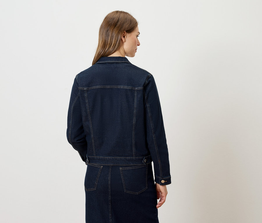 Rückansicht einer Frau, die eine dunkelblaue Jeansjacke und einen Rock trägt.