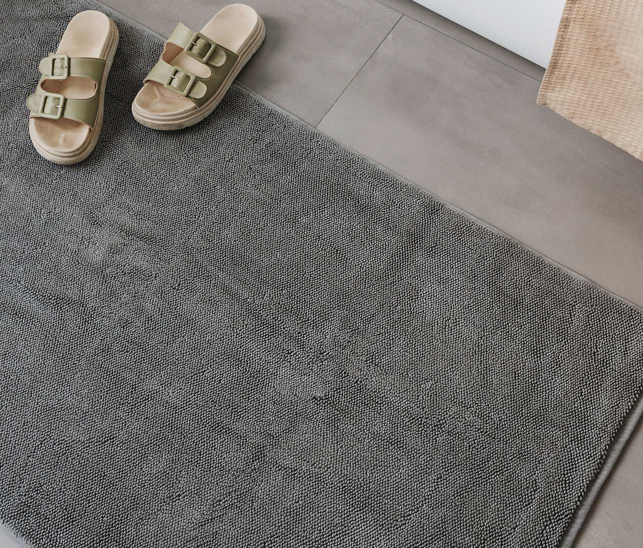 Eine graue, rechteckige Badematte »Ole« von benuta (70 x 120 cm) liegt auf einem Badezimmerboden, daneben Sandalen.