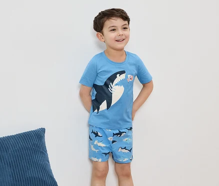 Ein lächelnder Junge trägt einen hellblauen Pyjama mit Hai-Motiv, vor einer weißen Wand.