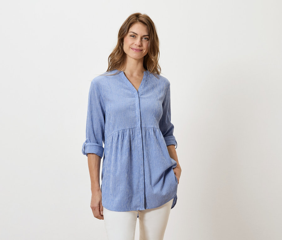 Frau trägt eine hellblaue, langärmelige Bluse und weiße Hosen.