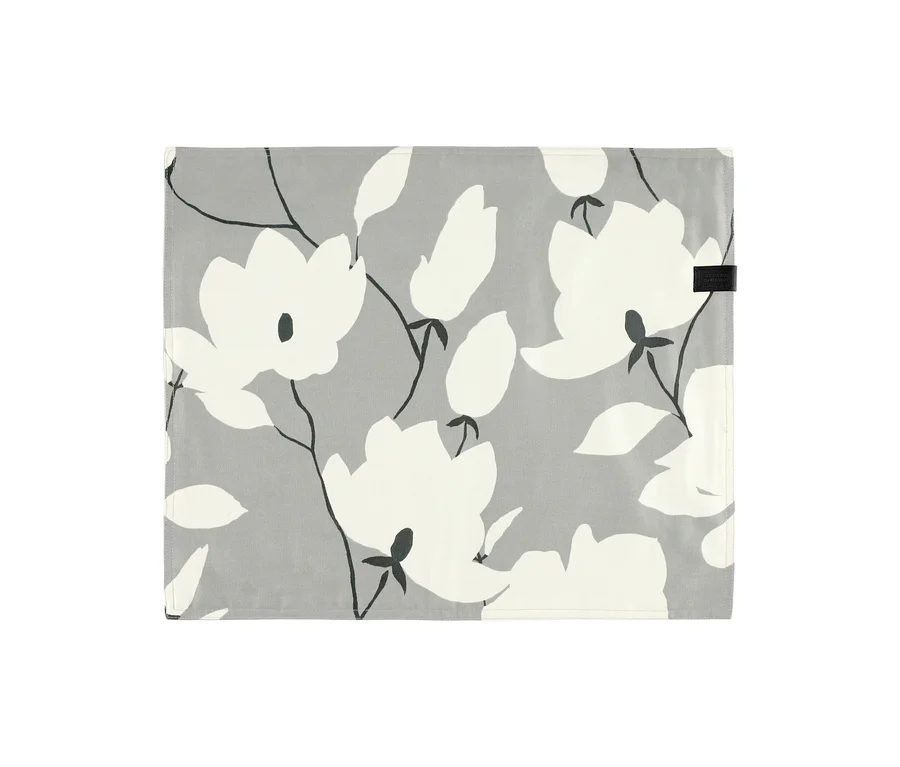 Grau-florales SCHÖNER WOHNEN Tischset mit weißen Blüten und dunklen Stielen, oben rechts mit schwarzem Etikett.