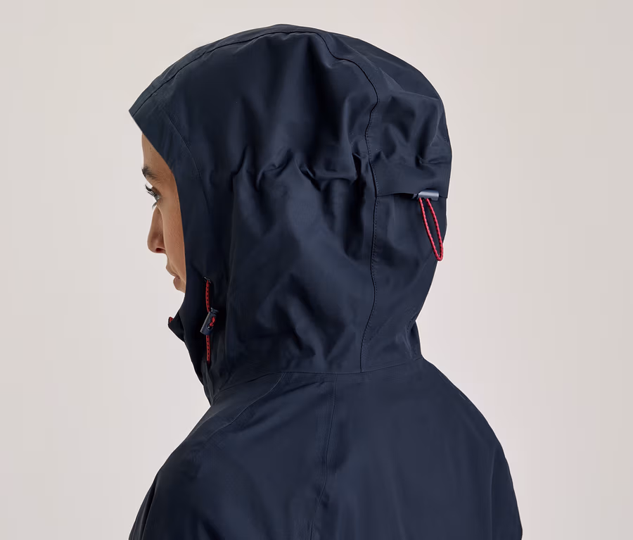 Person von der Seite, die eine dunkelblaue Kapuzenjacke mit hochgezogener Kapuze und roten Kordelzügen trägt.