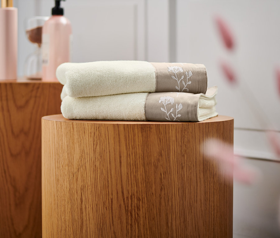 Gestapelte beige 2 Premium-Handtücher auf einem Holzsockel.