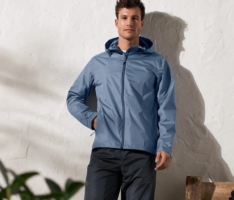 Mann steht und trägt eine blaue Unisex-Regenjacke.