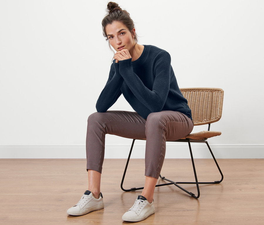 Frau sitzt auf einem Stuhl und trägt einen Strickpullover in Boucléoptik.