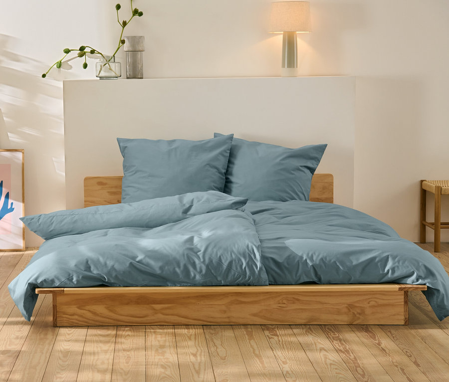 Blaue Perkal-Bettwäsche in Normal- und Übergröße auf einem Holzbett.