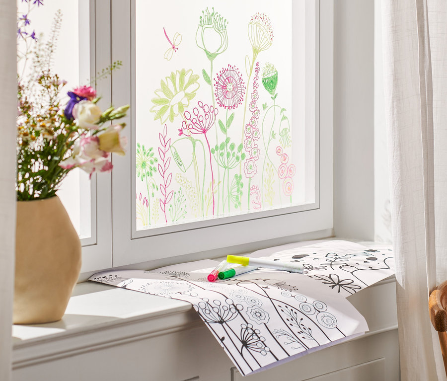 Blumen in Vase stehen auf Fensterbrett, Fenster ist bemalt und auf dem Brett liegen Oster-Fenstermalerei und Stifte.