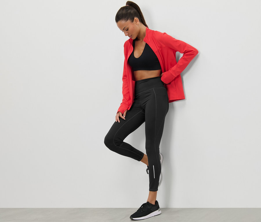 Frau posiert in schwarzen Sporttights und roter Jacke.