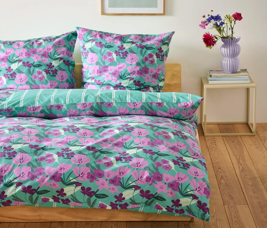 Mintgrüne Renforcé-Bettwäsche mit Blumenmuster auf einem Bett.