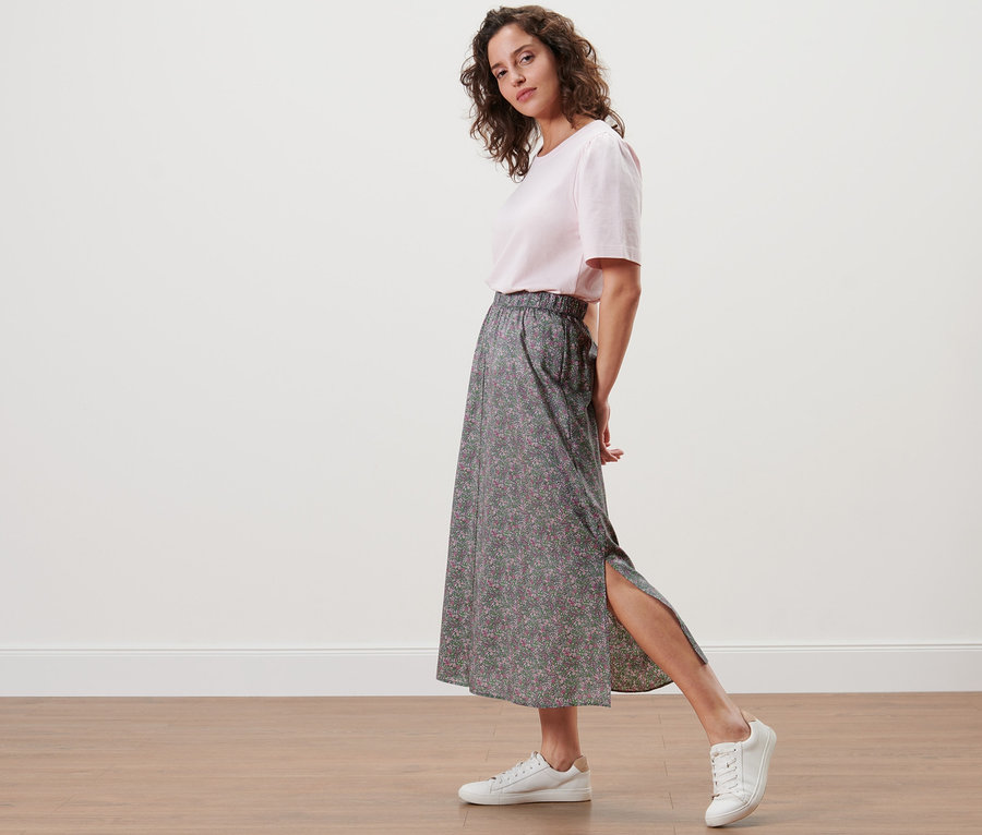 Frau posiert in einem floralen Midi-Rock und weißen Turnschuhen.