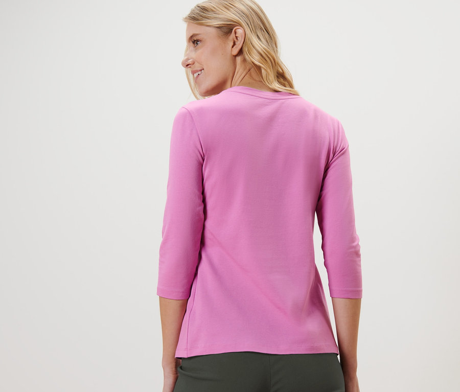 Frau blickt über die Schulter und trägt ein rosa Shirt mit 3/4-Arm.