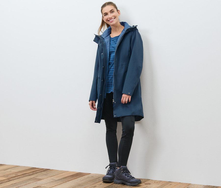 Eine Frau posiert in einem marineblauen 3-in-1-Funktionsmantel mit Weste.