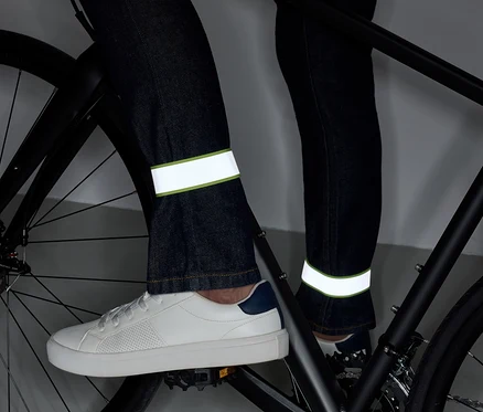 Beine auf einem Fahrrad in Jeans mit reflektierenden Streifen und weißen Schuhen.