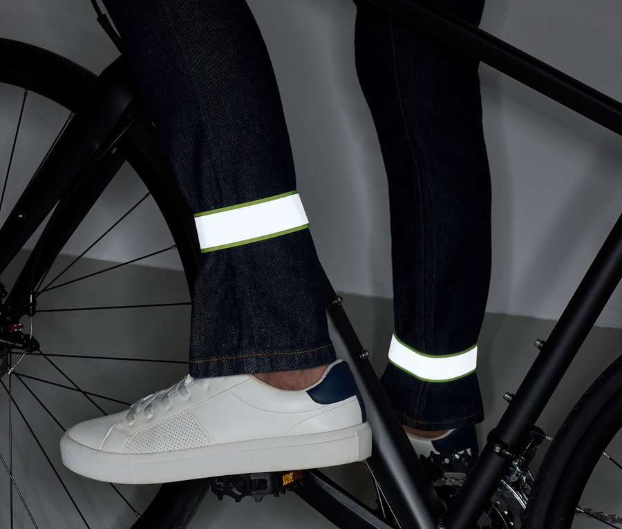 Beine auf einem Fahrrad in Jeans mit reflektierenden Streifen und weißen Schuhen.