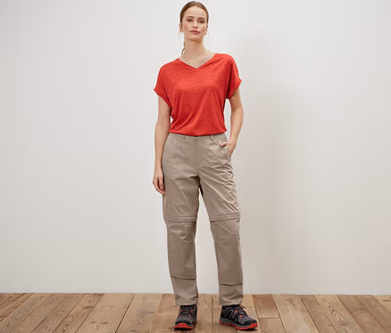 Eine Frau posiert in einer beigen 2-in-1-Funktionshose und einem roten T-Shirt.