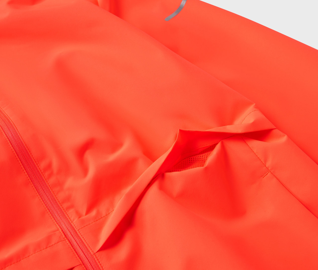 Detailaufnahme einer neonorangen Jacke mit Tasche und reflektierendem Streifen am Ärmel.