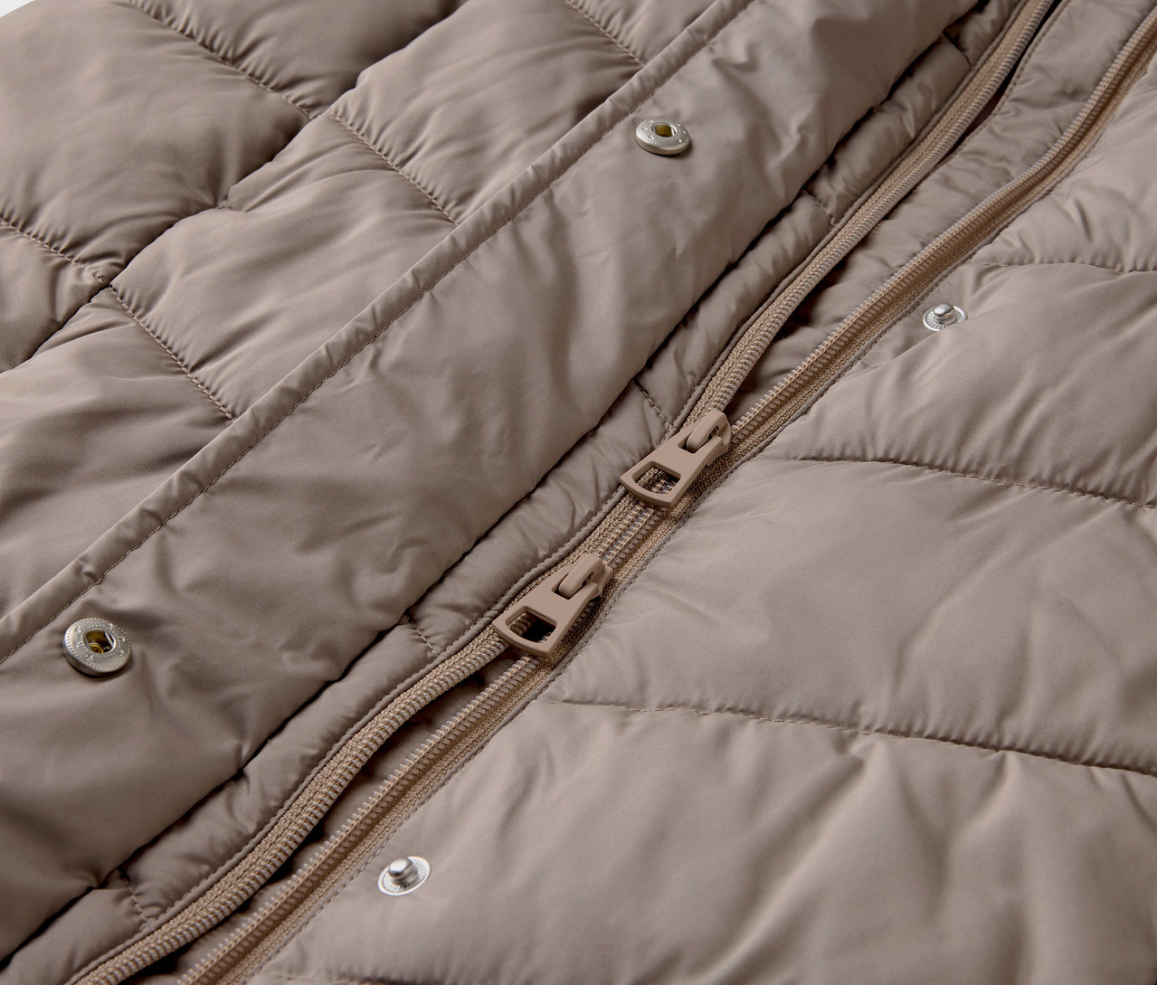Detail einer beigen Steppjacke mit Reißverschluss und Druckknöpfen.