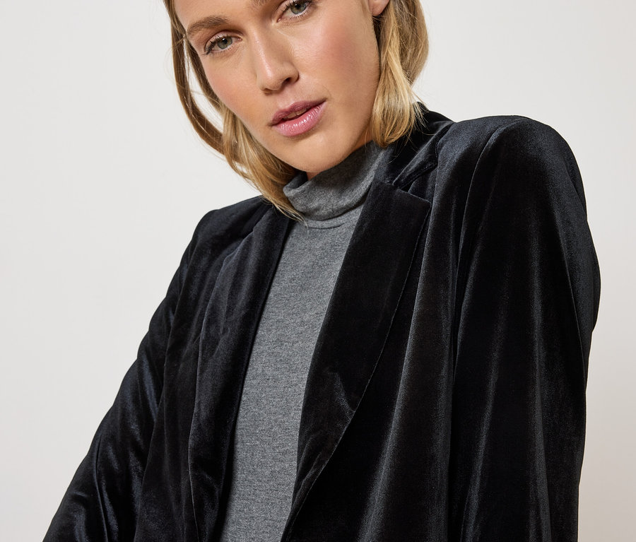 Frau trägt einen schwarzen Samtblazer und einen grauen Rollkragenpullover.