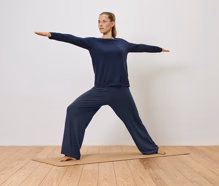 Frau in blauer Kleidung macht Yoga auf einer Matte.