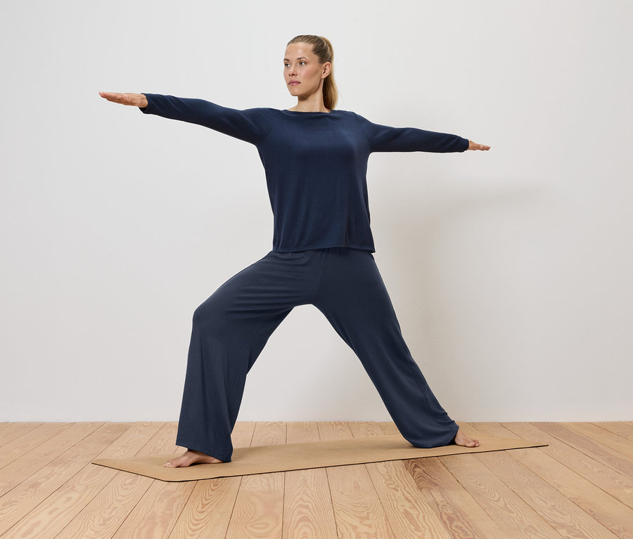 Frau in blauer Kleidung macht Yoga auf einer Matte.