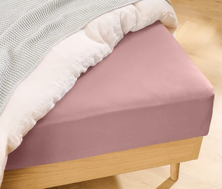 Rosafarbenes Jersey-Spannbettlaken auf einem Bett.