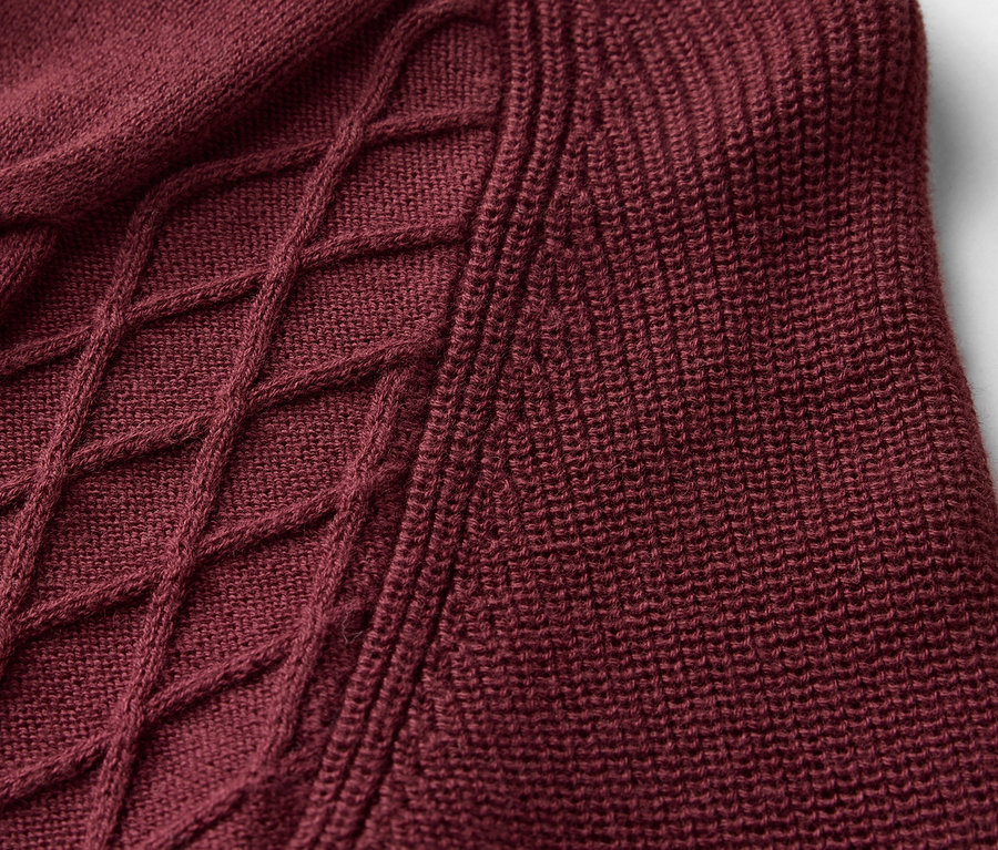 Detailaufnahme eines burgunderfarbenen Strickpullovers mit Zopfmuster.