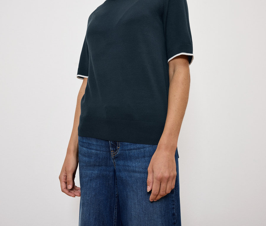 Frau trägt ein dunkelblaues Kurzarm-Top und blaue Jeans.