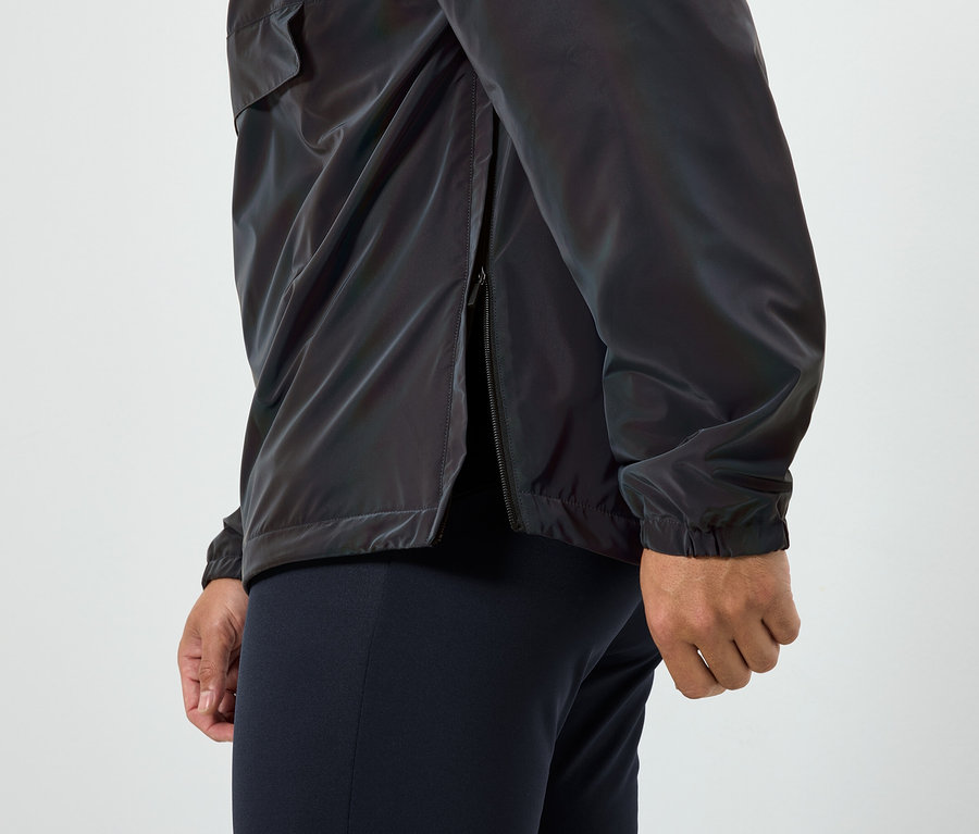 Mann trägt eine glänzende Jacke mit offenem Reißverschluss an der Seite und dunkelblaue Hosen.