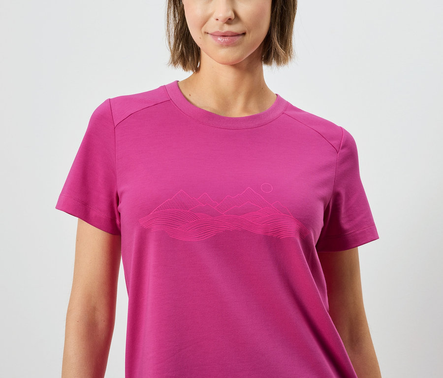 Frau trägt ein pinkes T-Shirt mit einer Berglandschaft darauf.