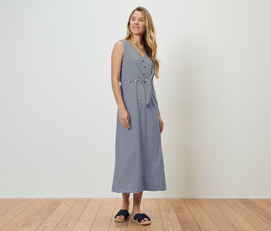 Frau steht in einem blau-weiß gestreiften Kleid und blauen Sandalen.