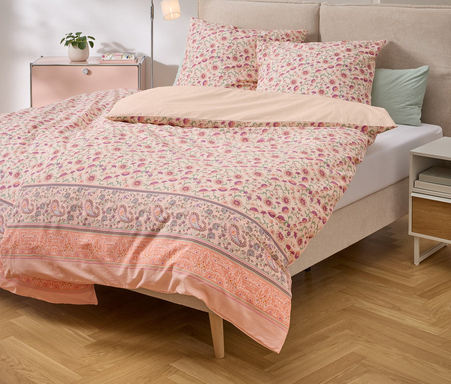 Bett mit rosa Blumenmuster-Bettwäsche und passenden Kissen auf einem Holzboden.