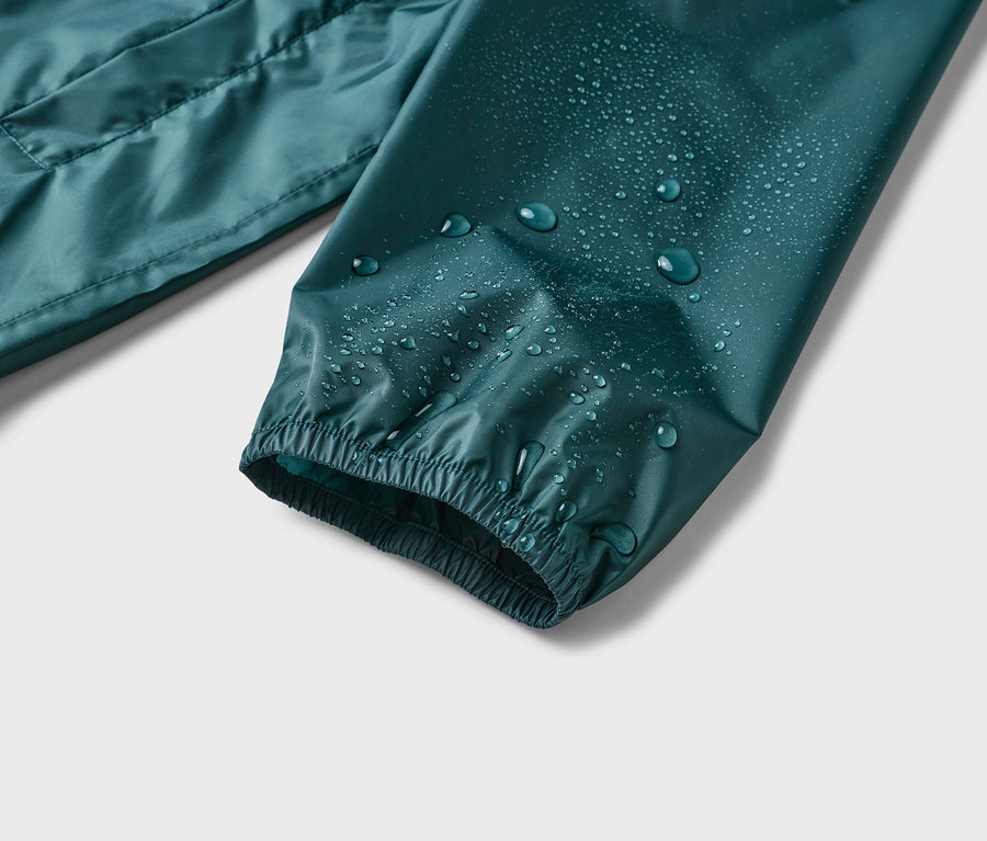 Nahaufnahme eines Ärmels einer wasserabweisenden, dunkelgrünen Jacke mit Wassertropfen darauf.