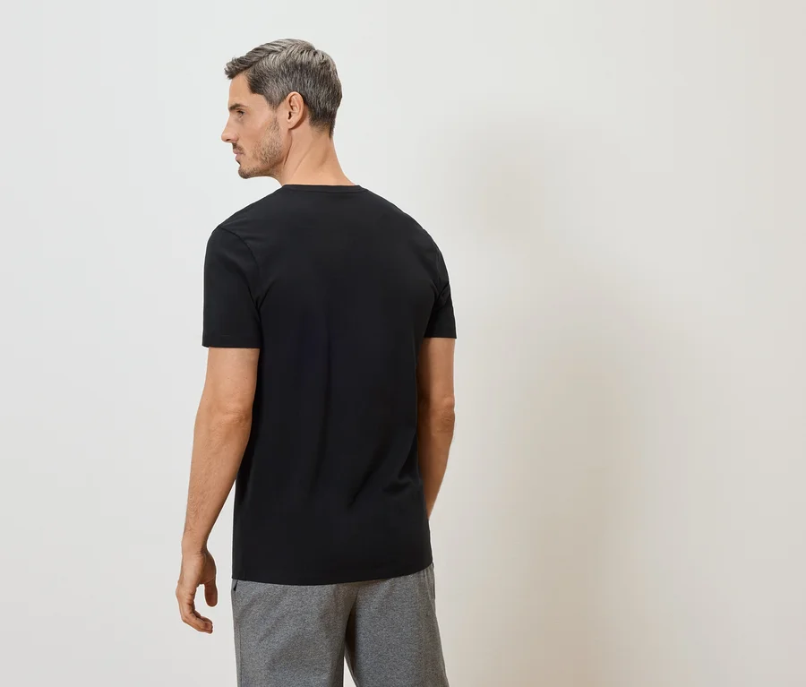 Mann von hinten in schwarzem T-Shirt und grauer Hose vor weißem Hintergrund.