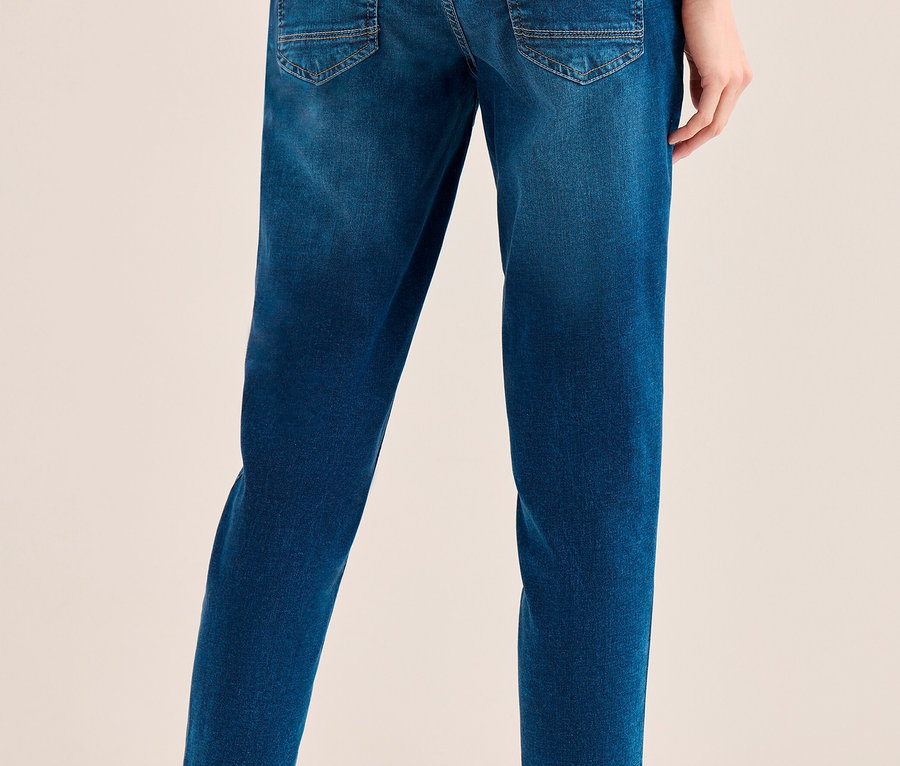 Eine Person von hinten, die eine blaue CECIL Jeans und weiße Sneaker trägt.