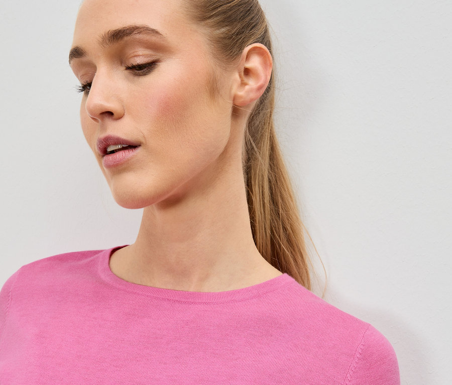 Nahaufnahme einer Frau mit blonden Haaren, die einen pinkfarbenen Pullover trägt.