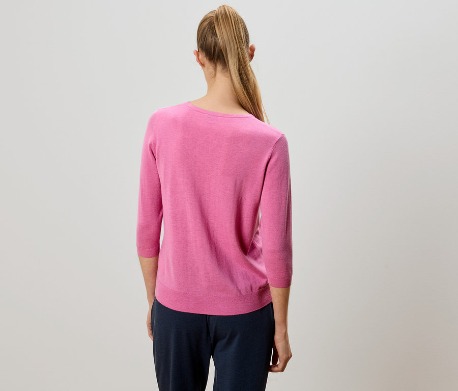 Rückansicht einer Frau mit blondem Pferdeschwanz, die einen pinkfarbenen Pullover und eine marineblaue Hose trägt.