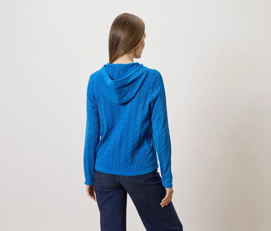 Rückansicht einer Frau mit langen, glatten Haaren, die einen blauen Zopfmuster-Hoodie und dunkle Jeans trägt.